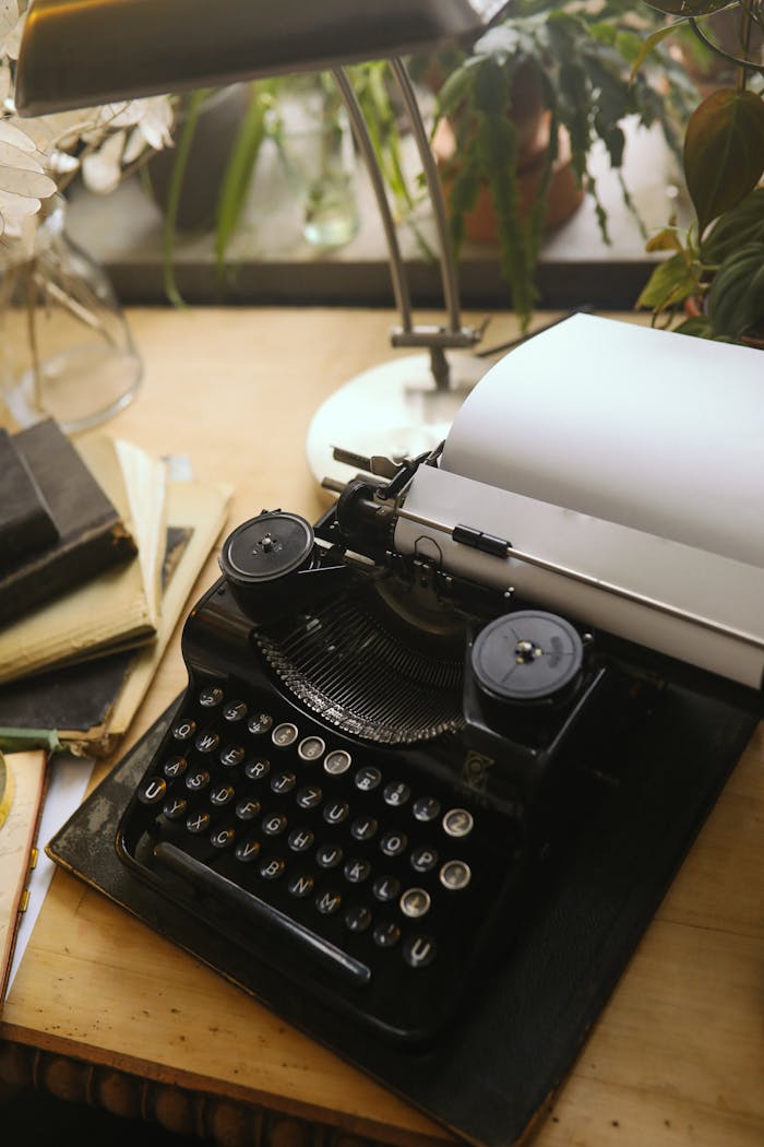 A classic black typewriter with paper and books on a wooden desk, illuminated by warm natural light.